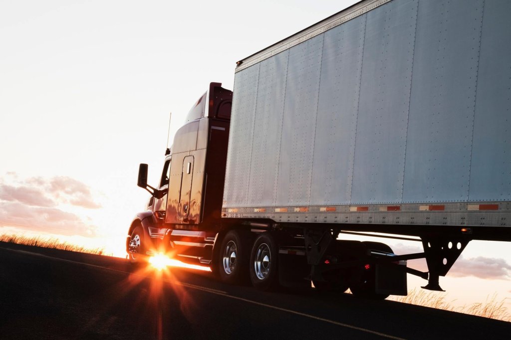 Silhouette of a commercial truck driving on a highway at sunset.